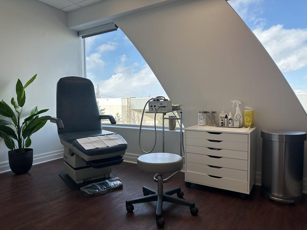 A bright treatment room at Aurora Foot Clinic & Orthotic Centre, with a treatment chair beside a large window and blue sky