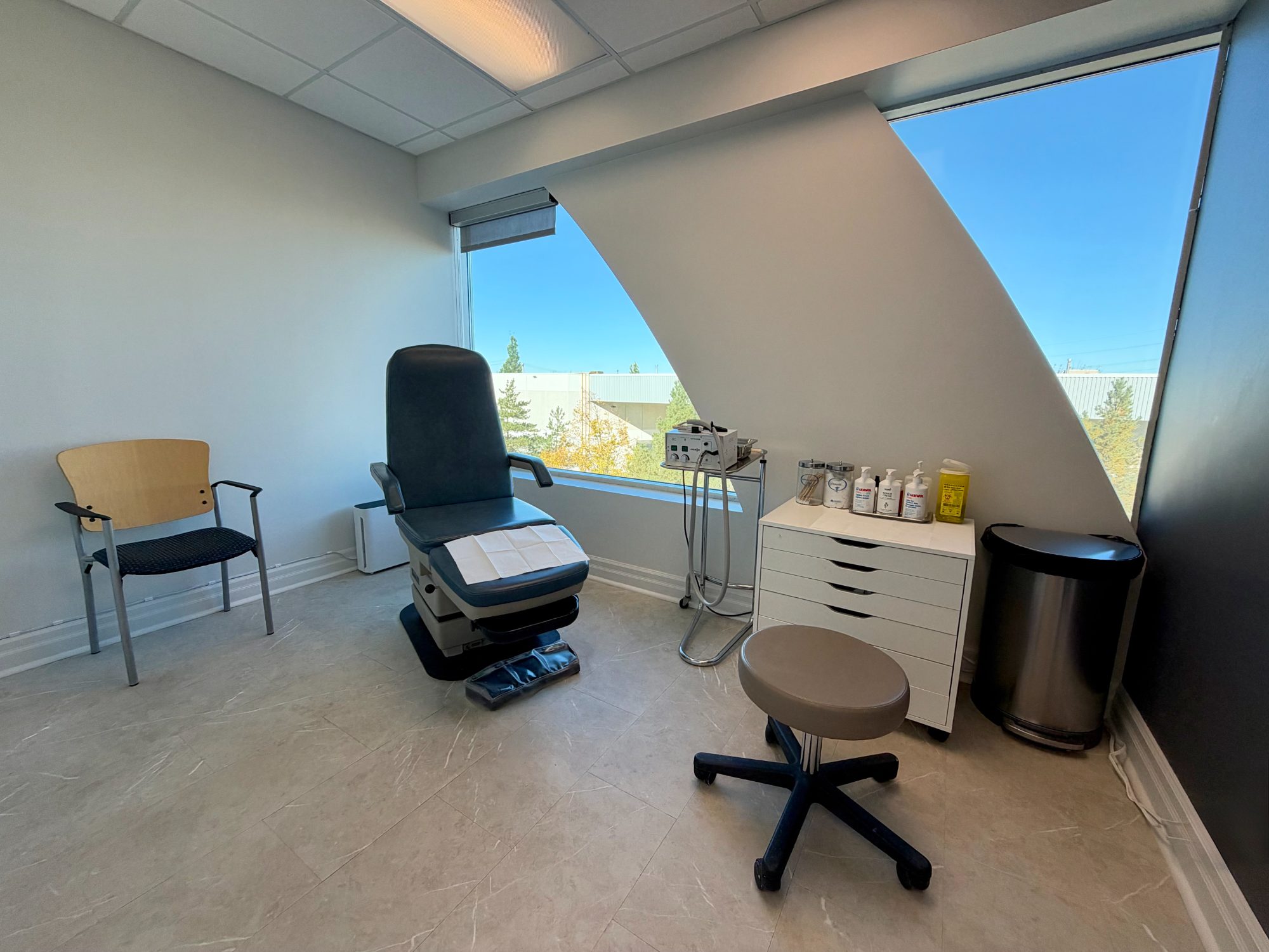 A bright treatment room with a treatment chair beside a large angled window